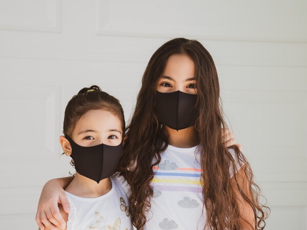 Two children wearing face masks, each child has one arm around the other child.